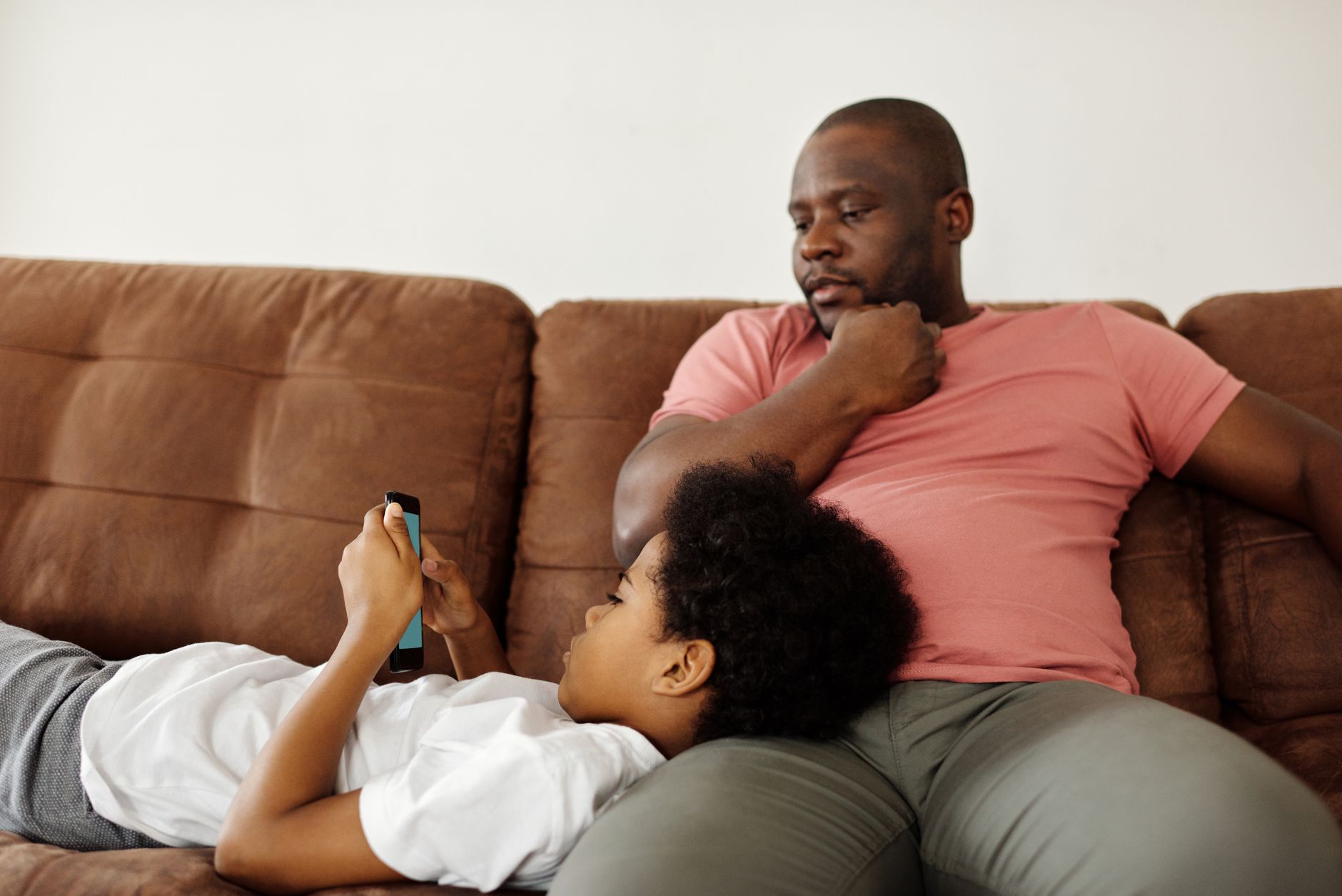 Un père et un enfant profitent de leur temps libre ensemble à la maison sur le canapé, concentrés sur un smartphone.