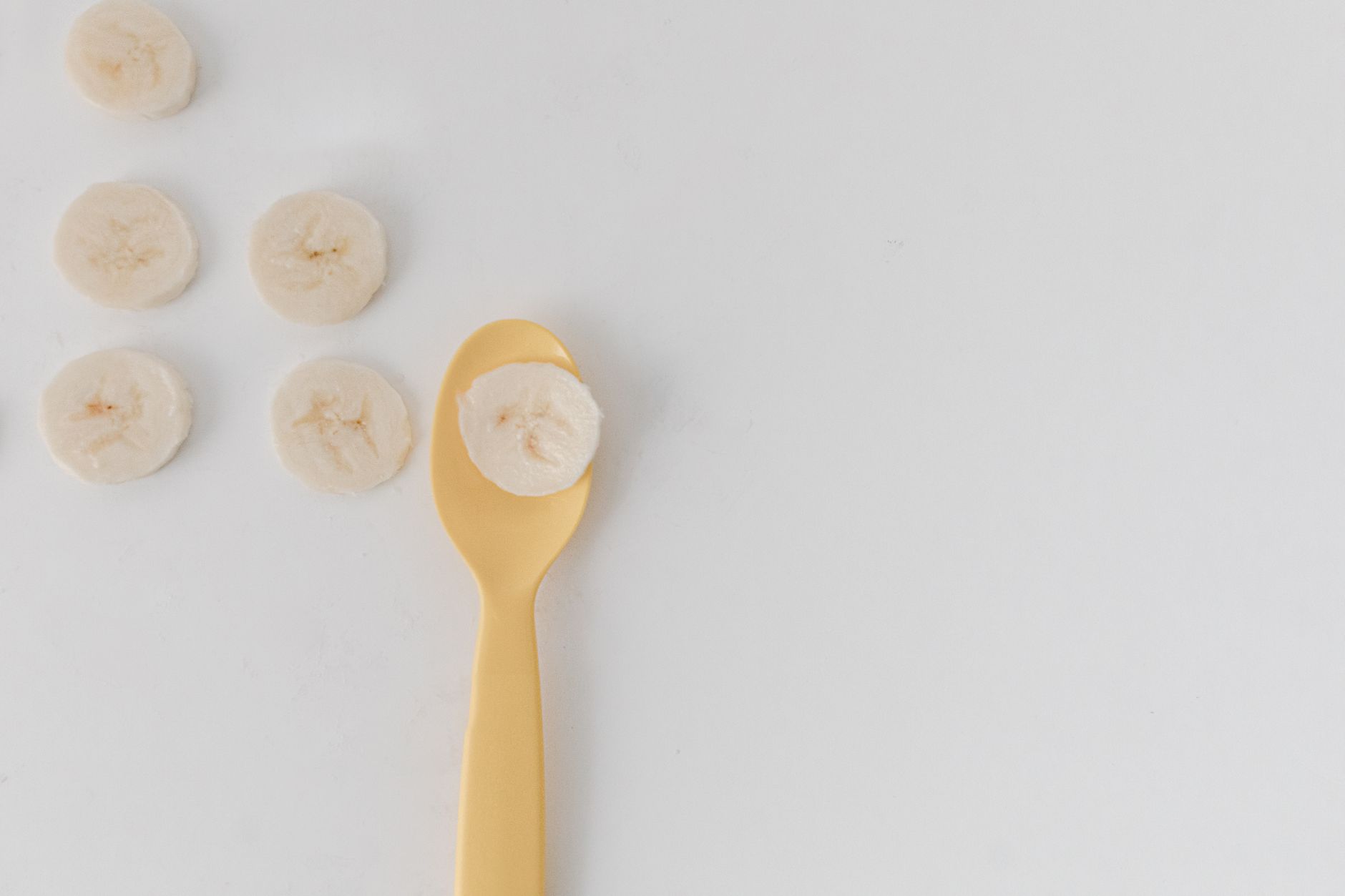 Rondelles de banane découpées sur un fond blanc, dont une posée sur une petite cuillère jaune.
