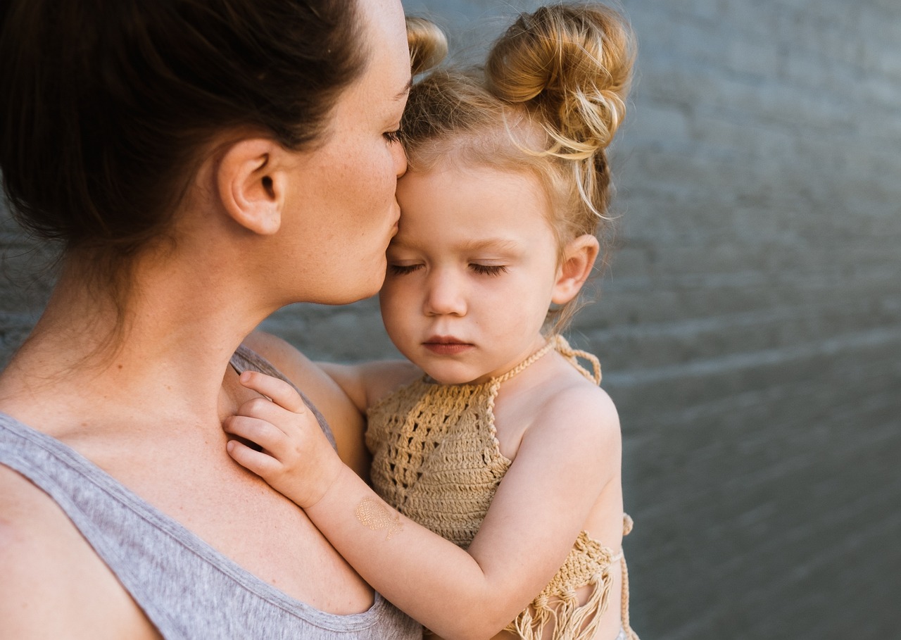 Une mère serre sa petite fille contre elle et l’embrasse sur la joue
